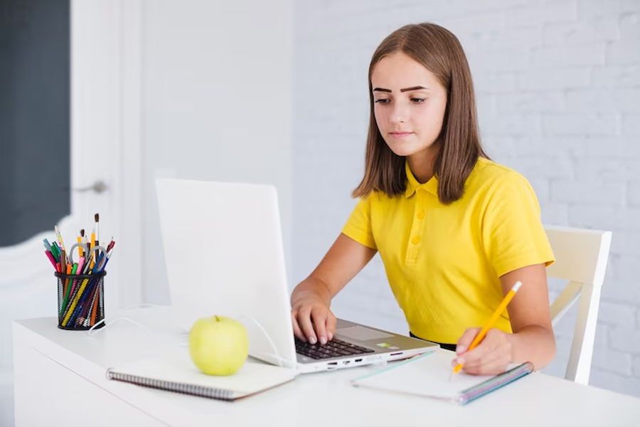 Девочка в желтой футболке сидит за столом и делает записи