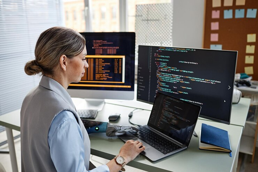 Девушка пишет код за столом с нотубуком и компьютером